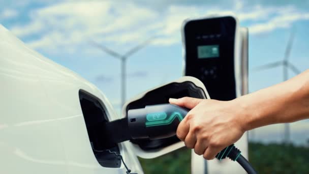 アジア人男性は 風力タービンによる充電ステーション電力から電気自動車にスマートEv充電器を挿入します Evとの持続可能なクリーン輸送技術のための将来の再生可能エネルギー利用 パーセント — ストック動画