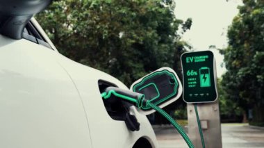 Doğal yeşil araba parkındaki ekolojik temiz enerji şarj istasyonundan gelen fütürist akıllı EV şarj aletinin şarj ettiği elektrikli araba. Alternatif enerji kullanan gelecekçi çevre dostu elektrikli araba. İnceleyin