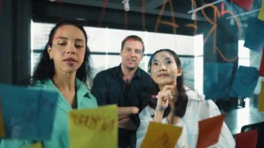 Profesyonel iş adamları, cam duvarda yaratıcı fikirleri paylaşmak için yapışkan notlar kullanarak pazarlama fikrini araştırıyor. Bir grup farklı iş adamları strateji hakkında tartışıyorlar. - Yakın çekim. Yönlendirici.