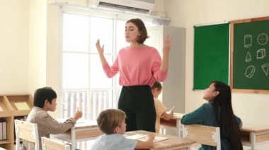 Beyazca öğretmeni, ilkokulda karatahta başında dururken vücut jesti kullanarak çok kültürlü öğrencilere teoriyi öğretiyor ve açıklıyor. Yetenekli öğretmen çocuklara soru soruyor. Pedagoji.
