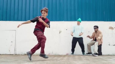 Genç Asyalı dansçı hip hop tarzında dans ediyor ve çok kültürlü arkadaşları duvarın arkasında tezahürat yapıyor. Çekici yakışıklı adam mavi arka planda kollarını uzatıyor. Açık hava sporu 2024 hiphop..