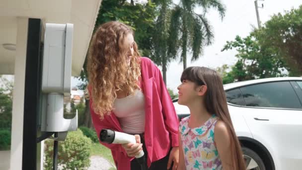 快乐的小女孩在家里的电动车充电站帮助妈妈给电动车充电时 学到了环保和能源可持续性 电动车和现代家庭观念 太奇怪了 — 图库视频影像