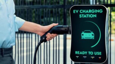 İşadamı EV şarj aletini şarj istasyonundan çıkarıp otoparktaki elektrikli arabayı şarj etmiş. CO2.Peruse 'u azaltmak için modern kentsel yaşam tarzı ve çevre dostu elektrikli araba kullanımı