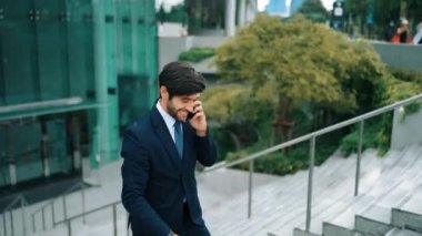 Gülümseyen yakışıklı iş adamı, parkın merdivenlerinde yürürken aynı zamanda işletme müdürünü arıyor. Yatırımcı işe giderken meslektaşıyla konuşuyor. Sevinçli..
