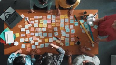 Akıllı iş adamlarının üst görüşü proje tasarımı hakkında toplantı odasında dizüstü bilgisayar ve yapışkan notlarla konuşur ve açıklar. Ayakta dururken logo tasarımının havadan görünüşü. Sempozyum.