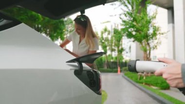 Yaz mevsiminde yeşil sürdürülebilir şehir bahçesinde ağır çekimde çalışan EV elektrikli araba yeşil sürdürülebilir şehirde yeniden şarj edilebilir elektrikli araç iç organları için alışveriş yapan genç çiftlerin yaşam tarzını gösteriyor.