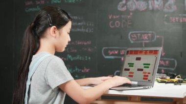 Genç mutlu Asyalı kız kodlama ve programlama tahtası başında. Lise öğrencisi, masada elektronik ekipmanlarla dizüstü bilgisayarı kullanarak mühendislik kodları yazıyor.