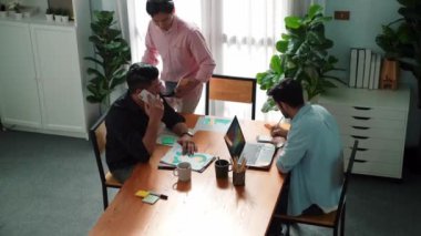 Proje yöneticisi toplantı odasında telefonla konuşurken beyin fırtınası fikriyle birlikte çalışan ekibin üst görüntüsü. Erkek lider yatırımcıyı arıyor ve ekip stratejisini tartışırken mevcut planı sunuyor. Cemaat.