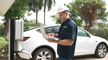 Evde EV şarj istasyonu kurulumu üzerinde çalışan nitelikli teknisyen, EV için dizüstü bilgisayarla şarj sisteminde sorun çıkarma ve yapılandırma ayarları yapıyor. Titiz