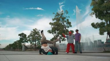 Profesyonel çekici hipster, Fountain ile sokak dansı yapıyor. Yakışıklı bir adamın B-boy ayak egzersizi sahnesi. Mavi arka plan. Modern yaşam tarzı. Açık hava sporu 2024. Yumuşak bir şekilde..