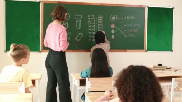アジアのスマートかわいい少年は教室で黒板に立っている間答えを書きます 小学校で数学のレッスンについて学び 学生を見ている若い美しい教師 教育コンセプト ペダゴロジー — ストック動画