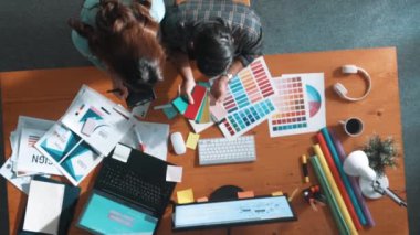 Akıllı tasarımcının renkli paletlerden renk seçmesine yardım ederken yukarıdan aşağı görünümü. Dizüstü bilgisayardan logoya bakarken birlikte çalışan ve planlayan iş adamlarının hava görüntüsü. Sempozyum.