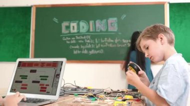 Kafkas arkadaşı STEM sınıfında elektrik panosunu tamir ederken Asyalı çocuk kodlama programı. Enerjik öğrenci kodlama mühendisliği komut yazarken ve yapay zeka yazılımını programlarken tahtada duruyor. Pedagoji.