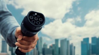 Kameranın önüne odaklanmış EV şarj cihazı bulanık şehir manzarası ve hızlandırılmış bulut arkaplanlı dijital akıllı batarya durum hologramını gösterir. Alternatif enerji kullanan EV araba şarjı. İnceleyin