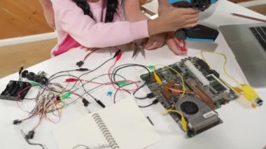 Akıllı öğretmen öğrencilere elektronik tahtayı öğretiyor. Kız dijital elektrikli aletleri ve ana kartı cips ve kablolarla tamir etmeyi öğreniyor. Masaya odaklan. Üst Manzara. Etkinlik.