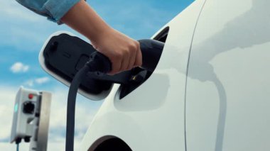 Asyalı adam şarj istasyonundan elektrikli arabaya akıllı EV şarj aleti takıyor. EV araba konseptiyle sürdürülebilir ve temiz ulaşım teknolojisi için gelecekteki alternatif enerji kullanımı. İnceleyin