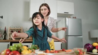 Zeki beyaz anne ve Asyalı kız birlikte yemek pişiriyor ve sebze doğruyor ya da akşam yemeği için salata hazırlıyor. Mutlu anne ve kız taze yemekle sağlıklı yemek yapıyorlar. Sağlıklı gıda konsepti. Pedagoji.