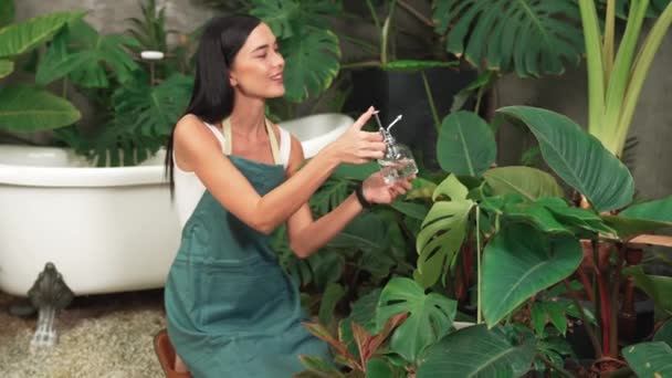年轻的女园艺师在简约的建筑风格 混凝土风格 夏季异国情调的植物叶园中照料热带植物 温和地浇灌热带植物 以家庭园艺为环保生活方式 — 图库视频影像