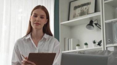 Klinikteki dost canlısı psikolog kadın. Profesyonel portresi. Kameraya bakıp psikolog muayenehanesine bakıyor. Tecrübeli ve kendinden emin psikolog.