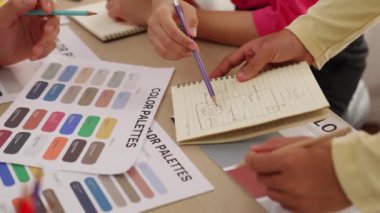 Not defterine yeni tasarım taslağı hazırlayan ve projeyi denetleyen müşteriyle renk seçimi yapan iki tasarımcının yavaş çekim çekimi. Tasarımcı bürosunda kromatik danışma. Değiştirilmiş