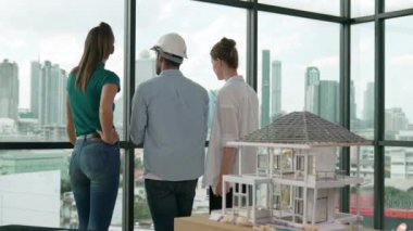 Gökdelene bakıp bir proje planı okurken, günlük kıyafetli akıllı mimar mühendis ekibi konuşuyor. Profesyonel yönetici takımı ev inşaatı hakkında beyin fırtınası yapıyor. Arkadan bak. İzleme