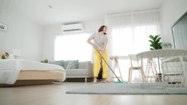 Modern apartman dairesinde dans ederken yerleri paspaslayan beyaz bir hizmetçi. Mutlu enerjik anne ya da temizlikçi müzik eşliğinde oturma odasını temizlemekten zevk alır. Yaşam tarzı. Pedagoji.