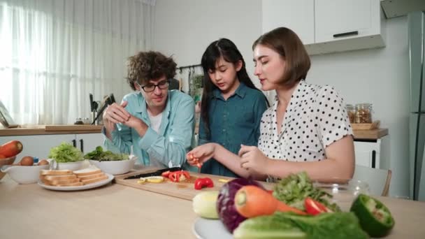 アジアの娘と新鮮な食事を調理するために 魅力的な白人のお父さんと母親は一緒に時間を過ごします エネルギッシュなパパとママは キッチンでサラダを作るために新鮮な野菜を準備しています 健康的な食べ物 ペダゴロジー — ストック動画