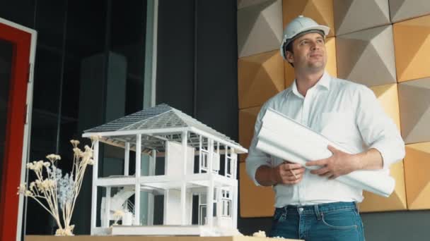 专业的高加索项目管理人员将项目计划与房屋模型放在桌面上 专业的建筑师工程师头戴安全帽 自信地站在那里 机械手 — 图库视频影像