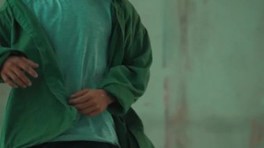 Hippi, şehir caddesinde hip-hop dinlerken kulaklık takıyor. Sokak dansçısı ayak seslerini kulaklıktan müziğe taşıyor. Açık hava sporu 2024. Çimento arka planı. Moda. Aktif stil. hiphop.