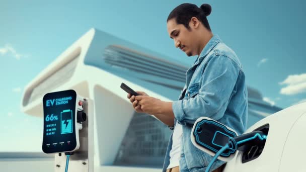 Azjata Czeka Używa Smartfona Podczas Gdy Jego Elektryczny Samochód Ładuje — Wideo stockowe