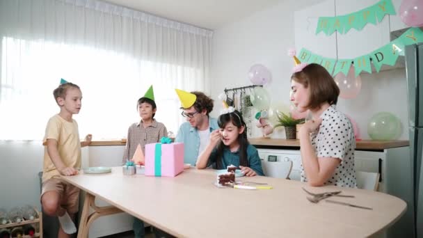 魅力的な家族は テーブルの上に置かれている間にカラフルな気球で装飾されたモダンなキッチンで話しながら娘の誕生日を祝います 幸せなアジアの女の子は笑顔の親とケーキを食べています ペダゴロジー — ストック動画