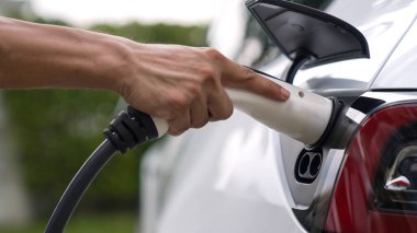 Modern çevre dostu adam EV şarj istasyonundan elektrikli aracı şarj ediyor. EV araba teknolojisi ev sakinleri için gelecekte çevresel sürdürülebilirlik için kullanılıyor. Eşzamanlama