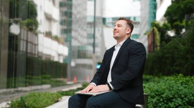 Kafkasyalı proje yöneticisi yeşil şehir merkezinde otururken dizüstü bilgisayardan ve kapalı laptoptan çalışmayı bitirdi. Yetenekli iş adamı rahat bir nefes alıyor ve bilgisayarını kapatıp yorgun gözlerini kapatıyor. Urbane.