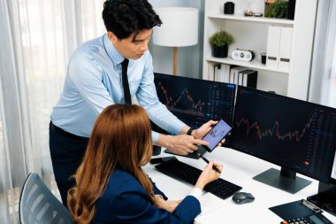 Gülümseyen işadamı cep telefonundaki dinamik borsa verilerini, iç ofisindeki internet sitesi uygulamasını analiz etmek için not yazan kadınlara gösteriyor. İnfobahn.