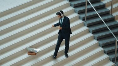Kulaklıktan müzik eşliğinde merdivenlerde duran profesyonel bir iş adamı. Merdivenlere dizüstü bilgisayar yerleştirip dans ederken dinlenme sesi dinleyen yetenekli bir proje yöneticisi. Modern dans. Sevinçli..