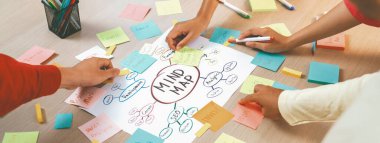 Profesyonel başlangıç grubu zihin haritası kullanarak yaratıcı pazarlama fikrini paylaşıyor. Genç yetenekli iş adamları yapışkan notlar yazarken beyin fırtınası planı yapıyorlar. Eline odaklan. - Yakın çekim. Değiştirilmiş.