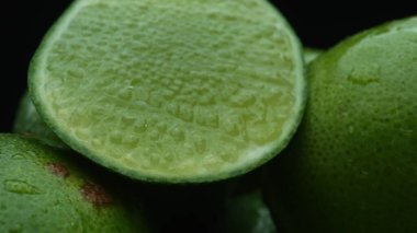 Limon dilimleri titizlikle bir yığın halinde, siyah arkaplana göre dizilmiş. Her bir kireç dilimi çarpıcı detaylar, canlı yeşil rengi ve baştan çıkarıcı dokusu ile yakalanır. Kapatın. Geliştirilebilir.