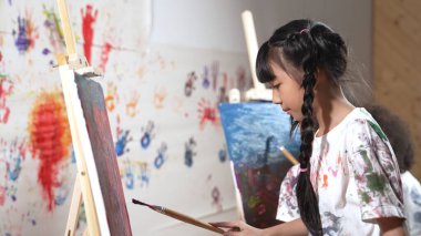 Oyuncu öğrenci resim yapıyor ya da resim dersinde çeşitli arkadaşlarla boyalı duvara resim çiziyor. Dağınık odada çalışan ya da sanat eserleri yaratan mutlu çok kültürlü çocuklar grubu. Yaratıcı aktivite. Etkinlik.