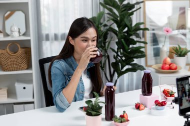 Gülümseyen, güzel Asyalı genç, lezzetli karışık çilek ve kiraz suyu detoksu içeceklerini inceleyen, sosyal medyada özel promosyon satışı için sağlıklı ürünler sergileyen. Taktik.