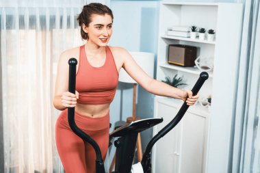 Spor ve atletik bir kadın, evdeki fiziğe ve sağlıklı spor yaşam tarzına uygun vücut egzersizi sırasında eliptik koşu makinesiyle koşuyor. Gaiety evde egzersiz eğitimi.