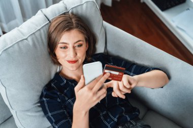 Genç mutlu kadın internetten alışveriş yaparak ürün satın alırken aynı zamanda internet üzerinden online ödeme sistemi ile çevrimiçi mağaza platformundan en yüksek siber güvenlik tarafından korunan ürünler sipariş ediyor.