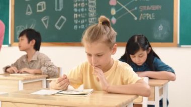 Stresli öğrenci, sınıfta çok kültürlü çocuklar yazarken ya da soruları cevaplarken tahtada otururken test yapmaya odaklanıyor. Becerikli öğretmen sınıf çalışmasını açıklıyor. Pedagoji.