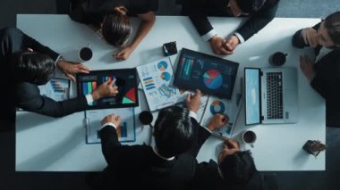 Akıllı proje yöneticisinin yukarıdan aşağıya hava görüntüsü, pazarlama ekibinin toplantı masasında dizüstü bilgisayar, tablet ve borsa mali istatistik belgeleriyle birlikte grafikleri analiz ederken büyüme grafiği sunar. Müdürlük.