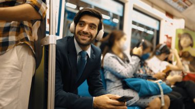 Gülümseyen yakışıklı yatırımcı trende otururken rahatlatıcı müzik dinliyor. Profesyonel iş adamı iş yerine toplu taşıma araçlarıyla giderken müzik dinlemeyi sever. Arka plan bulanık. Sevinçli..