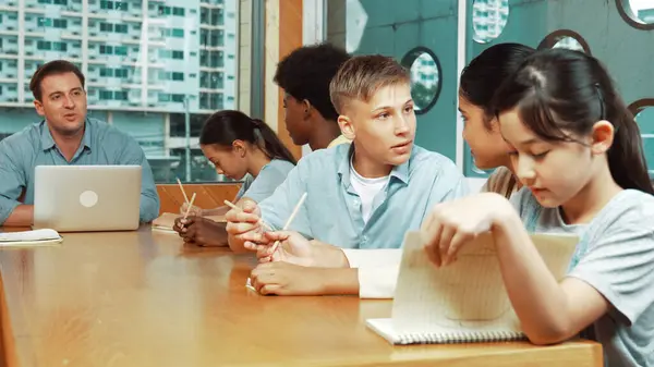 stock image Caucasian teacher and multicultural students clapping hand or putting the hand in the air together to celebrate for successful project with laptop and equipment placed on table in class. Edification.