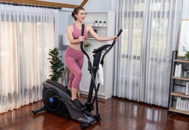 Spor ve atletik bir kadın, evdeki fiziğe ve sağlıklı spor yaşam tarzına uygun vücut egzersizi sırasında eliptik koşu makinesiyle koşuyor. Gaiety evde egzersiz eğitimi.