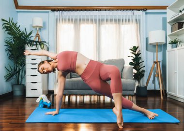 Spor kıyafetleri içinde esnek ve becerikli bir kadın evde egzersiz paspası üzerinde meditasyon pozisyonunda yoga yapıyor. Huzurlu ve huzurlu bir yoga yaşam tarzı..