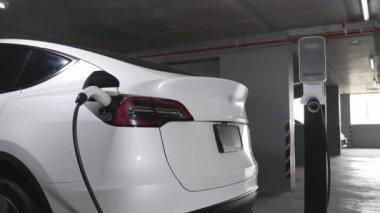 Şehir merkezindeki kapalı otoparkta yavaş çekimde EV elektrikli araba şarj oluyor. Şehir merkezinde sürdürülebilirlik yeşili, yeniden şarj edilebilir elektrikli araç iç organları.