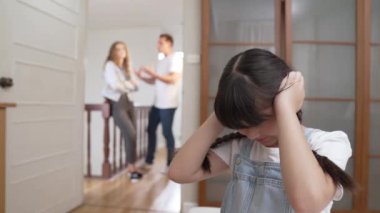 Stresli ve mutsuz genç kız köşeye kıvrılıp kulaklarını kapatarak arka planda ebeveyninin tartışmasını engelliyor. Evde aile içi şiddet ve travmatik çocukluk depresyona dönüşür. Titiz