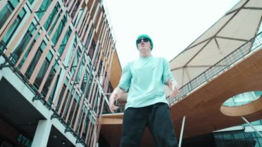 Kameraya bakan profesyonel beyaz sokak dansçısı. Genç, çekici bir adam, modern alışveriş merkezinde hip hop gösterisi yapıyor. Düşük açı. Serbest stil dansı. Açık hava sporu 2024 hiphop..